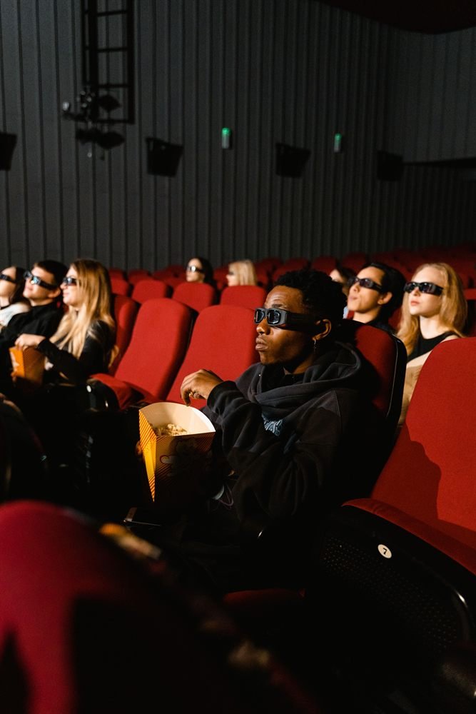 Moviegoers in 3D glasses with popcorn, watching in a dark theater